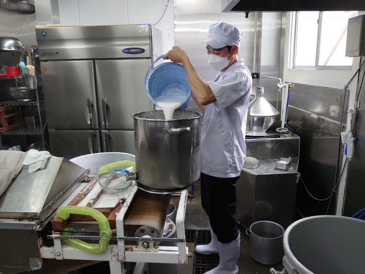 Nhân viên đang đổ bột vào nồi nguyên liệu trên máy Nhân viên đang đổ bột vào nồi nguyên liệu trên máy